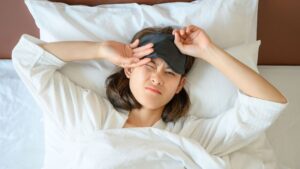 High angle view of young woman hate to wake up in the morning and she wearing sleep mask during sleeping on the bed.