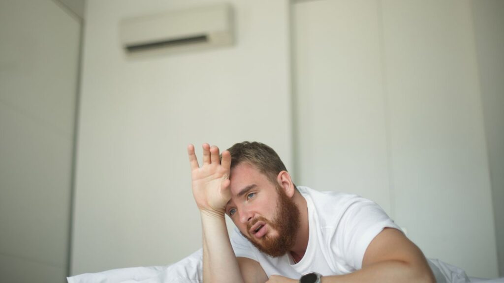 Young,Bearded,Man,Using,Air,Conditioner,At,Home,,Lay,On