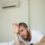 Young,Bearded,Man,Using,Air,Conditioner,At,Home,,Lay,On