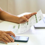 Close-up view of a woman calculating house bills with a mobile phone.